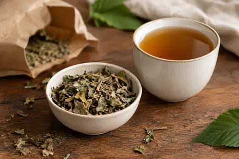 Feuilles de mûrier blanc en vrac près d’une tasse d’infusion ambrée sur un comptoir en bois