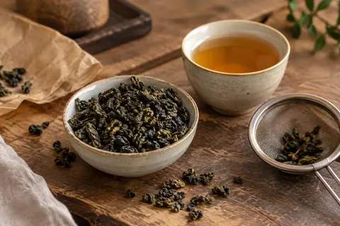 Feuilles entières de thé oolong dans un bol en céramique, avec une tasse et une passoire
