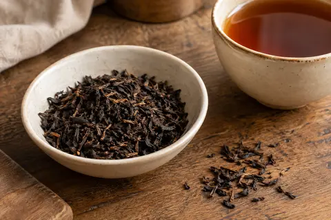 Feuilles de thé noir Assam en vrac dans une coupelle, avec une tasse d’infusion ambrée