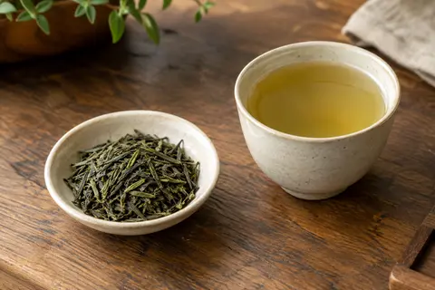 Feuilles de thé vert Sencha près d’une tasse infusée, posées sur un comptoir en bois patiné