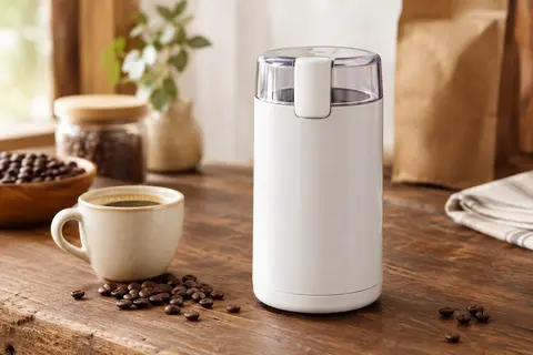 Moulin à café Bosch blanc posé sur un comptoir en bois, avec quelques grains de café et une tasse
