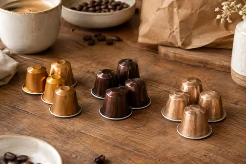 Capsules de café en aluminium présentées en trois groupes sur un comptoir en bois patiné
