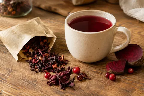 Tasse d’infusion rouge aux baies, avec un sachet en papier et des ingrédients sur un comptoir en bois.