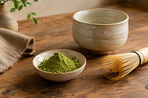 Poudre de matcha vert dans une céramique claire, avec un bol et un fouet à thé en bambou.