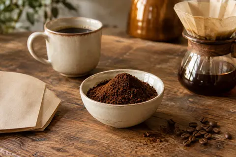 Café moulu brun dans une coupelle en céramique, près d’un filtre posé sur un comptoir en bois.