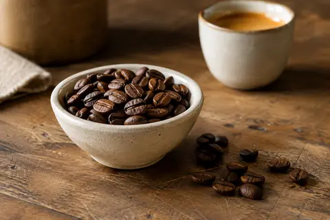 Grains de café Kimbo Espresso Classico dans une coupelle en céramique sur un comptoir en bois