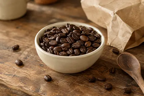 Grains de café entiers torréfiés dans une coupelle en céramique sur un comptoir en bois