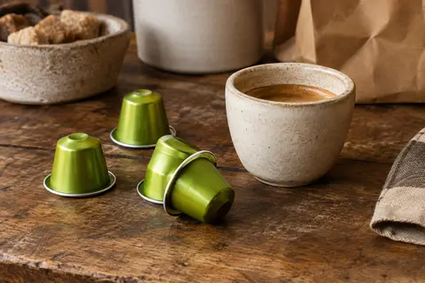 Capsules XXL en aluminium vert limone disposées près d’une tasse de ristretto sur un comptoir en bois