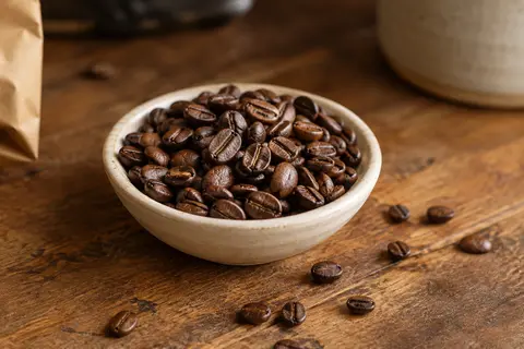 Grains de café torréfiés présentés dans une coupelle en céramique sur un comptoir en bois