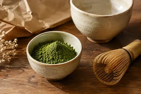 Poudre de matcha vert dans un bol en céramique, avec un fouet posé sur un comptoir en bois.