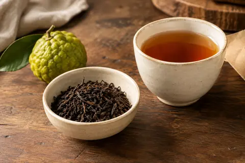 Feuilles de thé noir Blue Earl Grey en vrac dans un bol, près d’une tasse d’infusion ambrée.