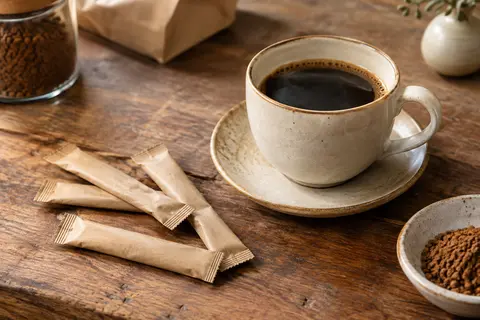 Sticks de café soluble décaféiné disposés à côté d’une tasse sur un comptoir en bois
