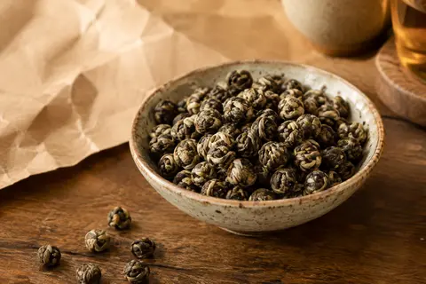 Feuilles roulées de thé oolong Jin Xuan, couleur sable, présentées dans une coupelle en céramique