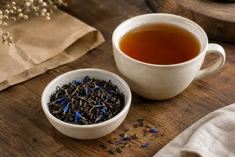 Thé noir Earl Grey en feuilles avec pétales de bleuet, présenté près d’une tasse ambrée
