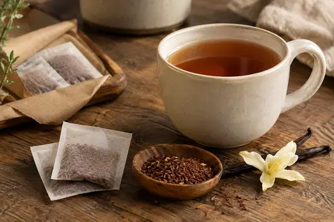 Tasse ambrée de rooibos à la vanille accompagnée de sachets individuels sur un comptoir en bois