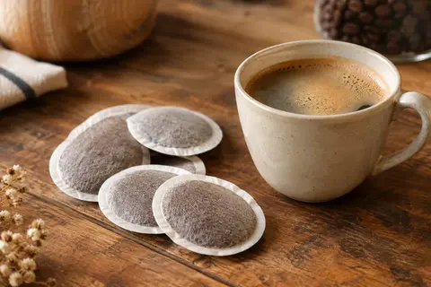 Dosettes de café Senseo Classique près d’une tasse à la mousse légère sur un comptoir en bois.
