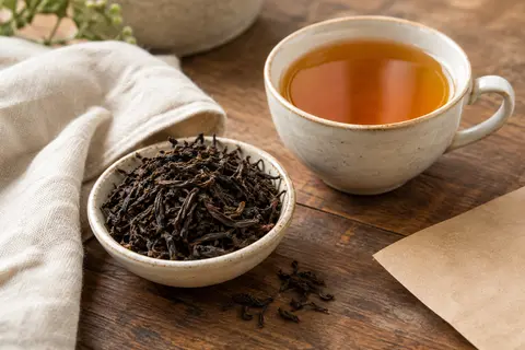 Feuilles de thé noir de Ceylan près d’une tasse d’infusion ambrée sur un comptoir en bois.