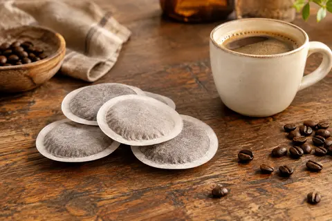 Dosettes de café Tassimo posées sur un comptoir en bois près d’une tasse de café long