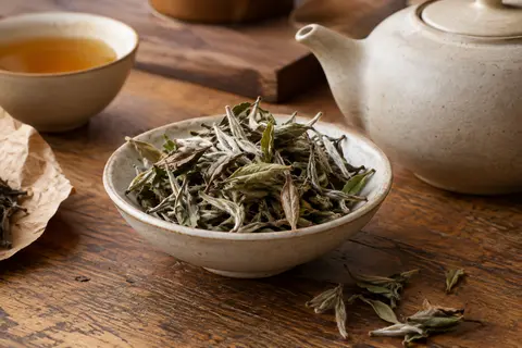 Feuilles de thé blanc Bai Mu Dan en vrac dans une coupelle en céramique sur un comptoir en bois